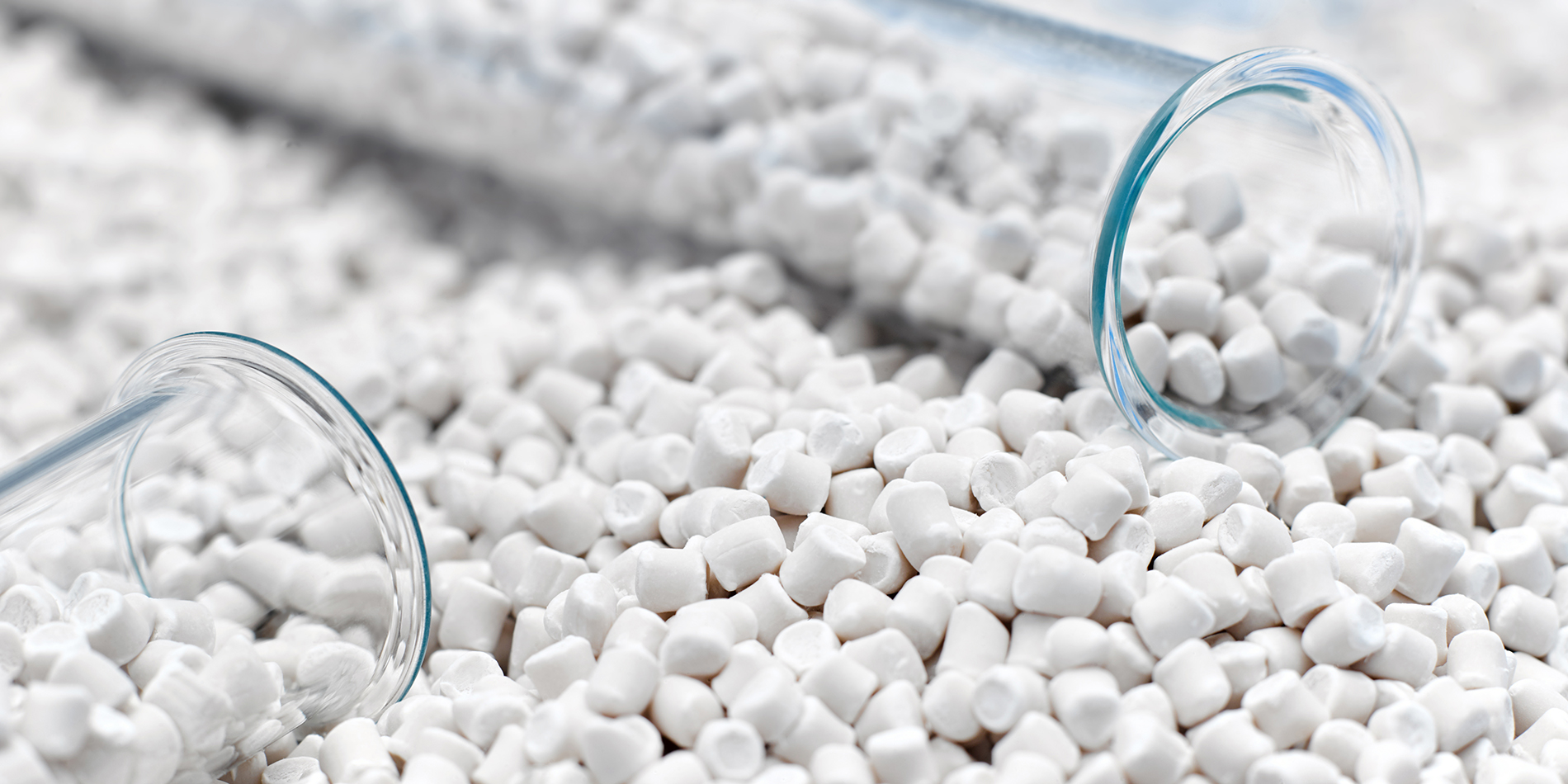 White plastic resin pellets spilled from laboratory glass tubes, illustrating the role of dual specification in ensuring material consistency and supply chain reliability in the modern plastics industry.