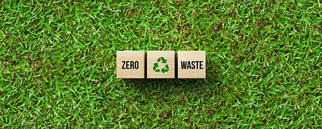 Wooden blocks on green grass displaying the words “Zero Waste” with a recycling symbol, representing sustainability efforts and zero‑waste packaging initiatives in the plastics industry.