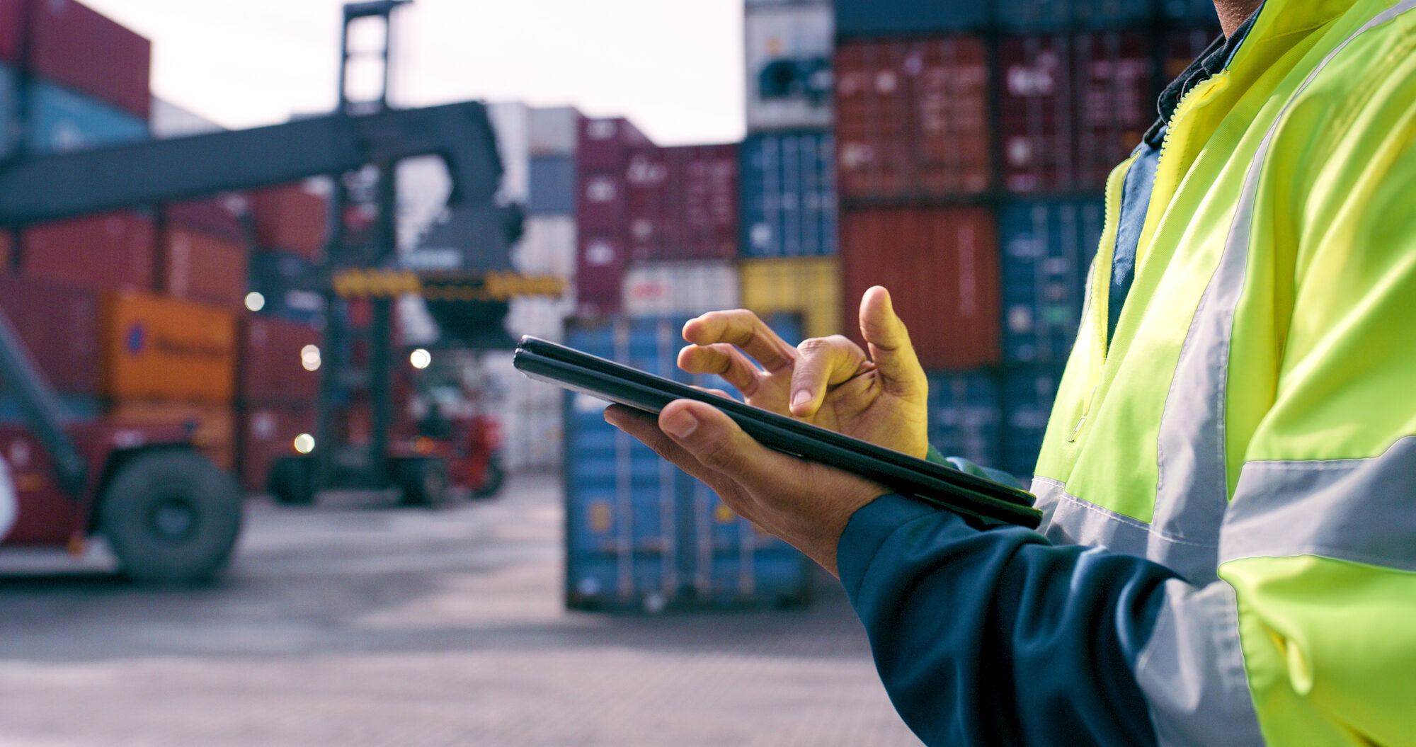 Worker using a digital tablet in front of shipping containers, highlighting real‑time supply chain monitoring for a smarter resin purchasing strategy in 2026.